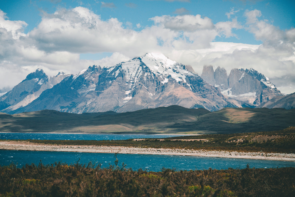 Snow-capped mountain peaks above a turquoise lake and scrubland in Chile