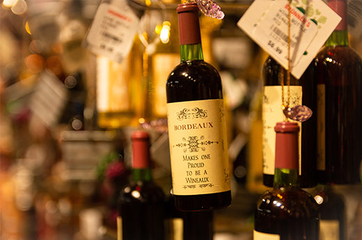 Bottles hanging with tags in a shop, one labeled "Bordeaux makes one proud to be a wineaux"