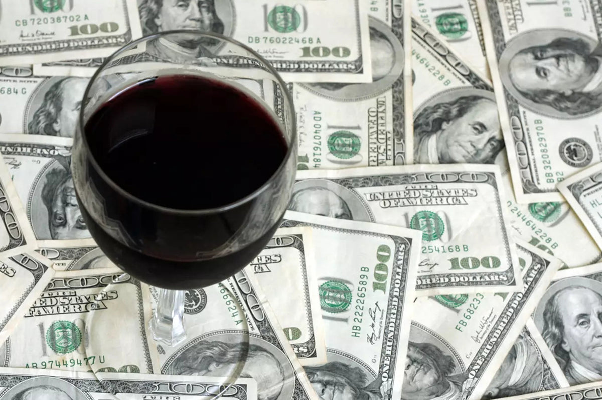 Glass of red wine standing on a spread of US hundred-dollar bills