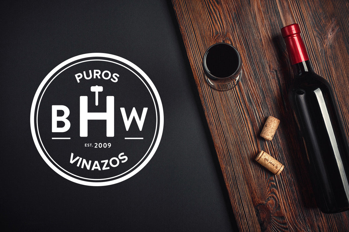 Puros Vinazos BHW logo beside a red wine bottle, a glass of wine and corks on a dark wooden table
