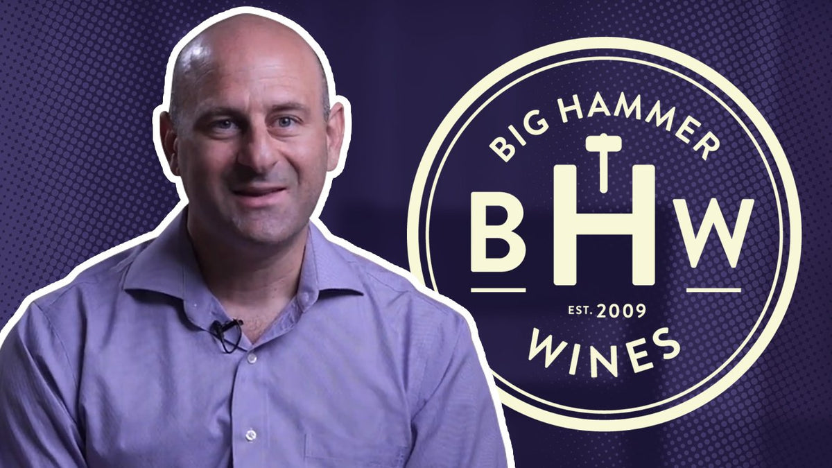 Man in a purple shirt smiling beside the Big Hammer Wines logo on a purple background