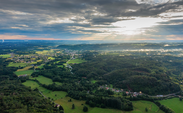 Aerial view of rolling green farmland and villages under sun rays breaking through clouds