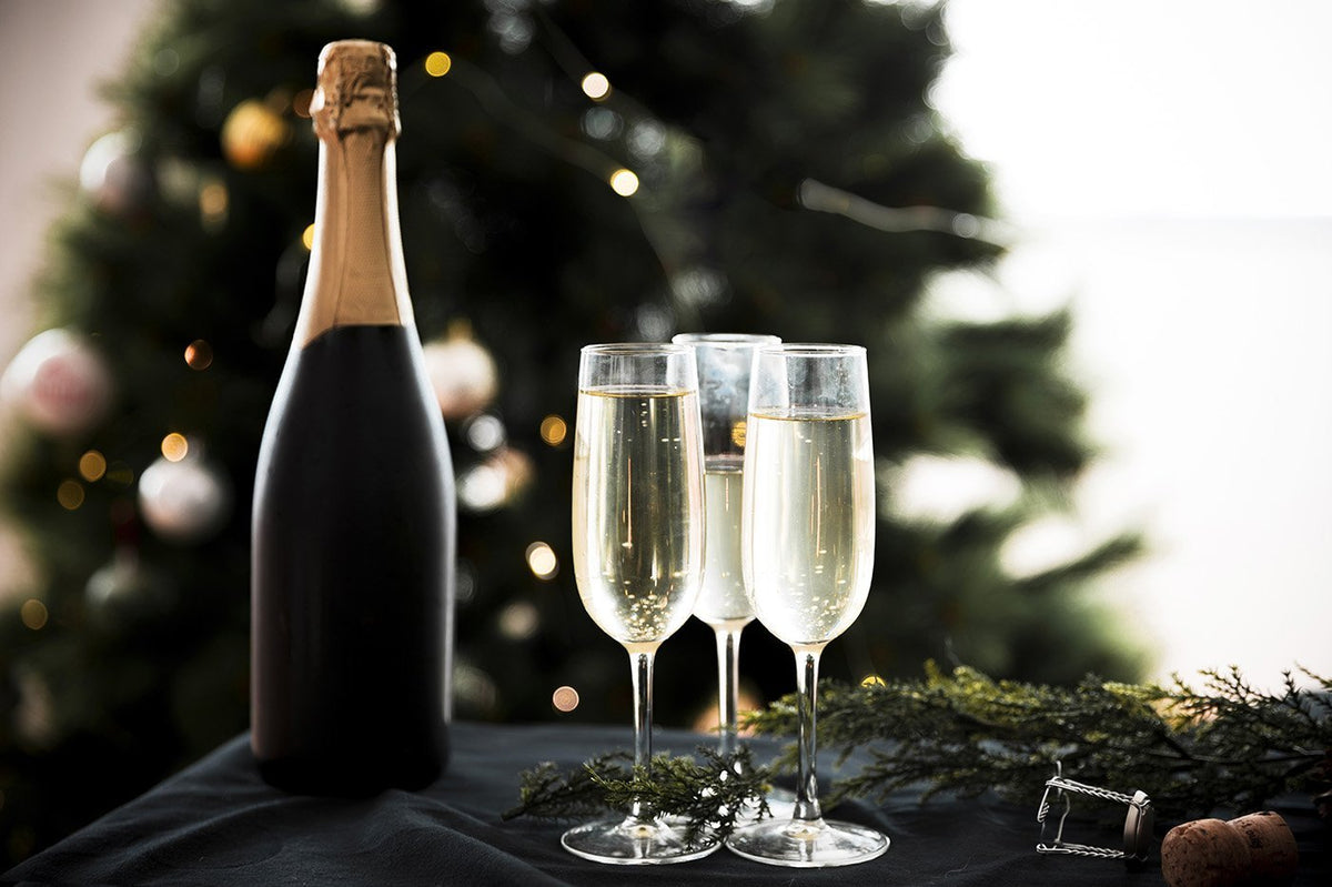 Bottle of sparkling wine and two filled flutes in front of a lit Christmas tree