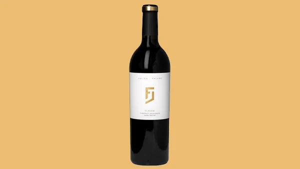 Bottle of Cabernet Sauvignon with a white label and a gold FJ monogram, on an orange background