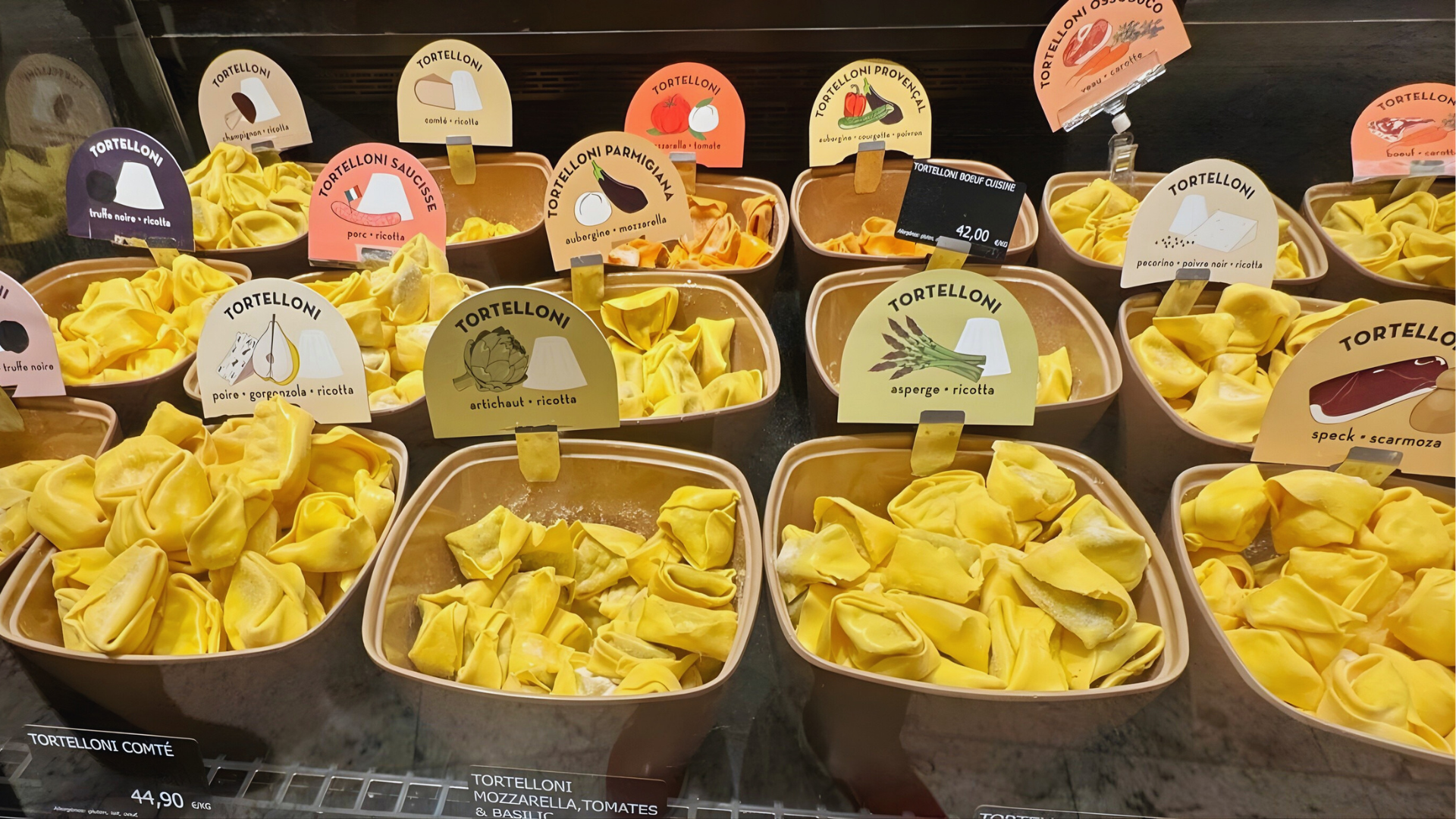 Assorted fresh tortelloni at an Italian pasta counter, including ricotta, artichoke, and truffle varieties.