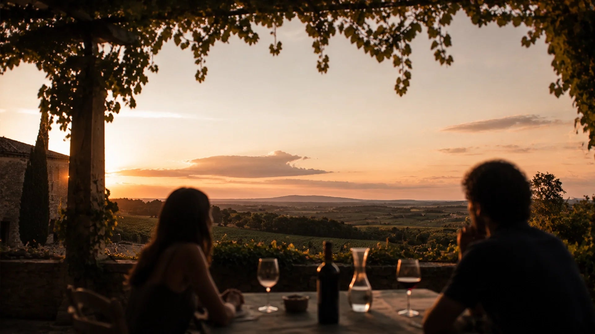 A couple sitting at a dining table with wine, enjoying a sunset view over the Rhône Valley vineyards.
