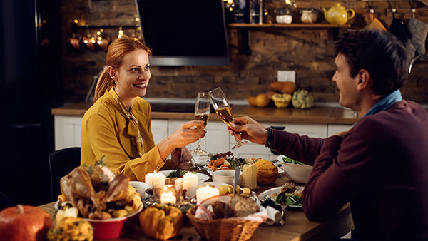 Couple toasting glasses of white wine at a candlelit table set for a holiday meal