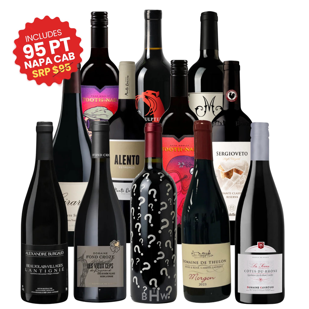 An assortment of 12 red wine bottles from the "Adventures in Wine" Wine Club, featuring various labels including a bottle covered in question marks and a red sticker highlighting an included 95-point Napa Cabernet, curated by big hammer wines.