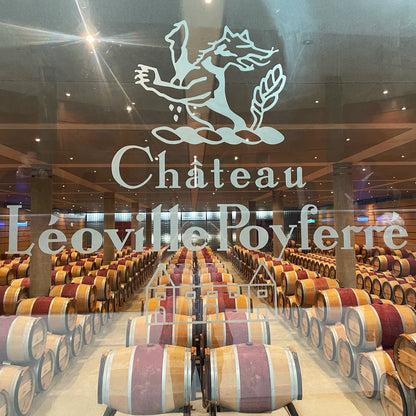 Château Léoville Poyferré winery logo etched on glass in front of a vast cellar filled with oak barrels, showcasing the estate’s winemaking process