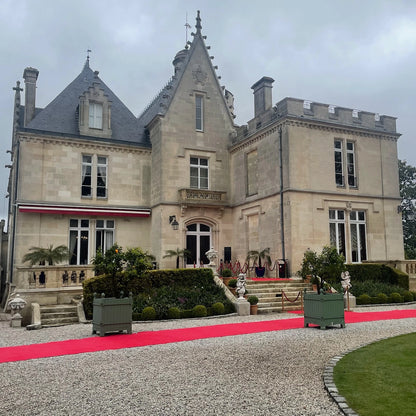 Château Pape Clément, a prestigious Bordeaux winery, with its grand château facade, red carpet leading to the entrance, and beautifully landscaped grounds