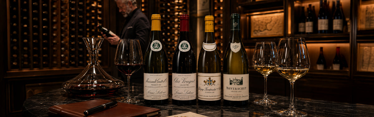 Four fine Burgundy wine bottles lined up on a marble table with wine glasses, a decanter, and a wine expert inspecting bottles in a dark cellar.