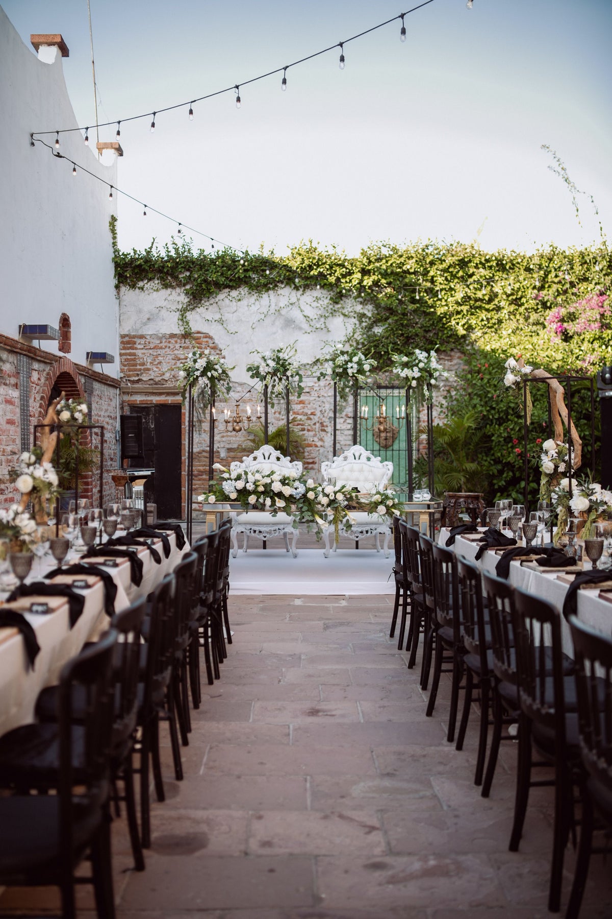 Elegant courtyard wedding reception with long tables under string lights